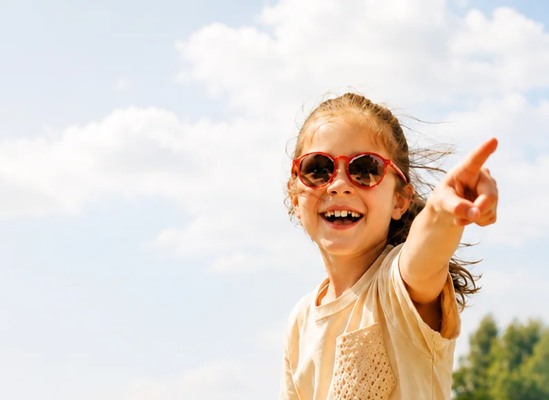 Lachendes Mädchen mit roter Kindersonnenbrille zeigt an der Küste in die Ferne