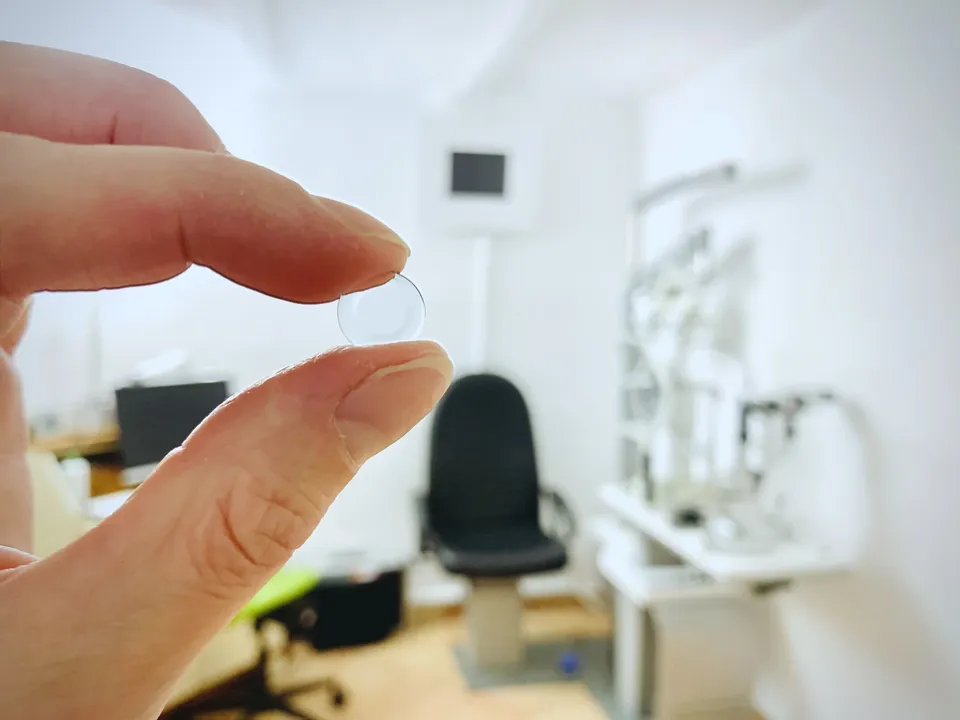 Formstabile Kontaktlinse zwischen zwei Fingerspitzen im Untersuchungsraum